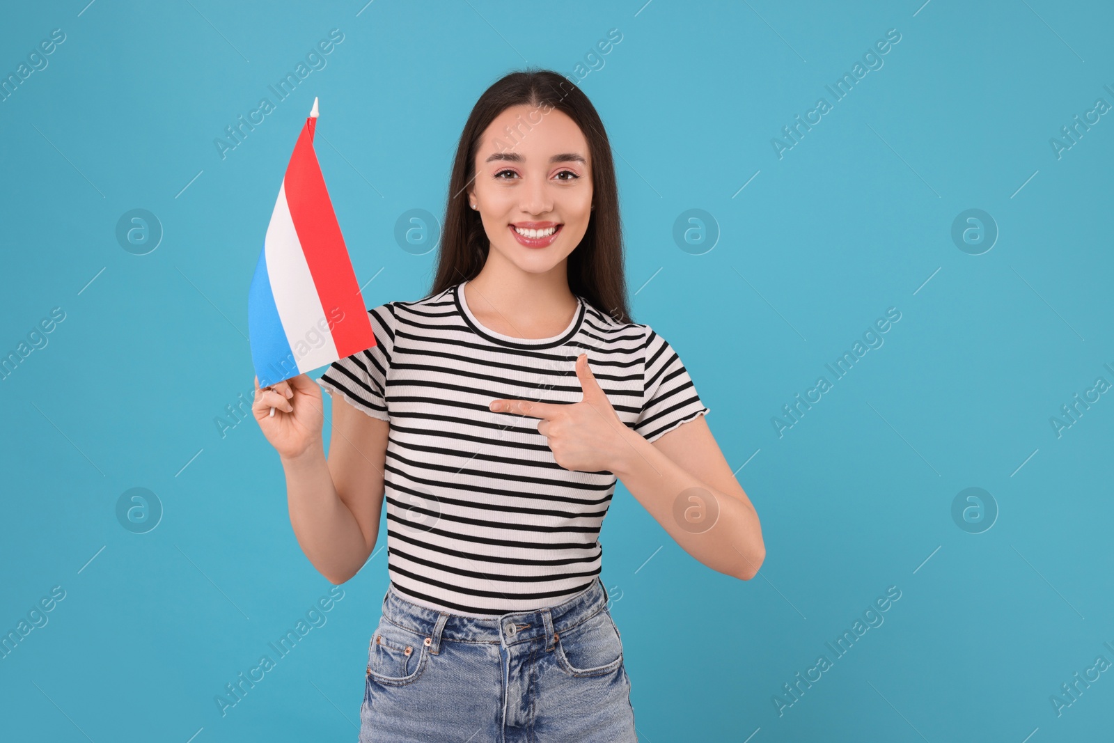Photo of Young woman holding flag of Netherlands on light blue background