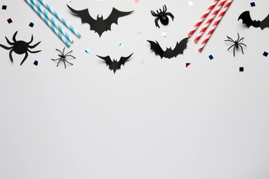Photo of Flat lay composition with paper bats, spiders and straws on white background, space for text. Halloween celebration