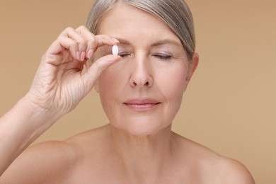 Beautiful woman with vitamin pill on beige background