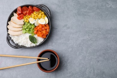 Photo of Delicious poke bowl with different ingredients, chopsticks and soy sauce on grey table, flat lay. Space for text