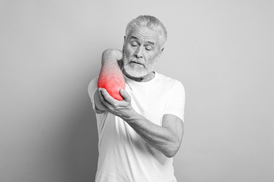 Image of Arthritis symptoms. Man suffering from pain in his elbow on grey background. Black and white effect with red accent in painful area