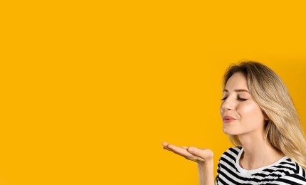 Photo of Portrait of happy young woman with beautiful blonde hair blowing kiss on yellow background