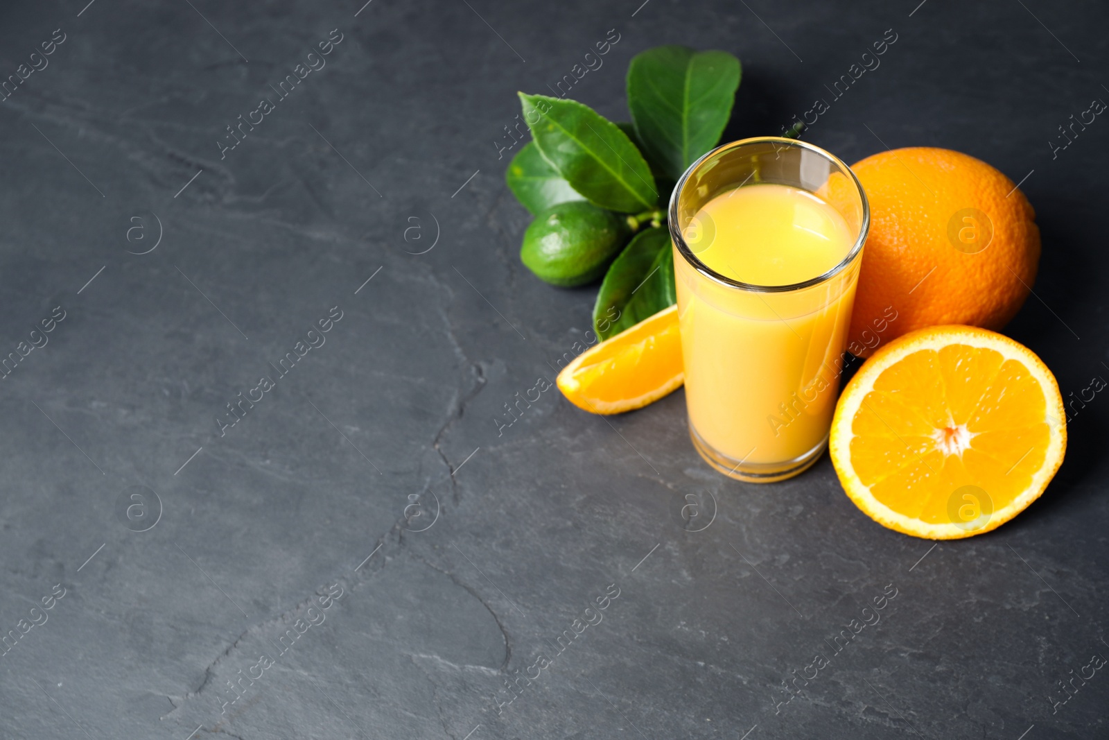 Photo of Glass of orange juice and fresh fruits on grey table. Space for text