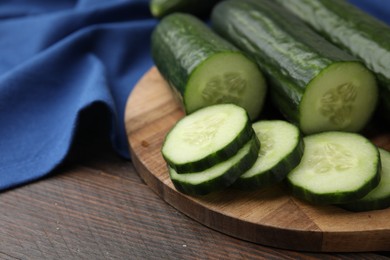 Photo of Fresh whole and cut cucumbers on wooden table, closeup