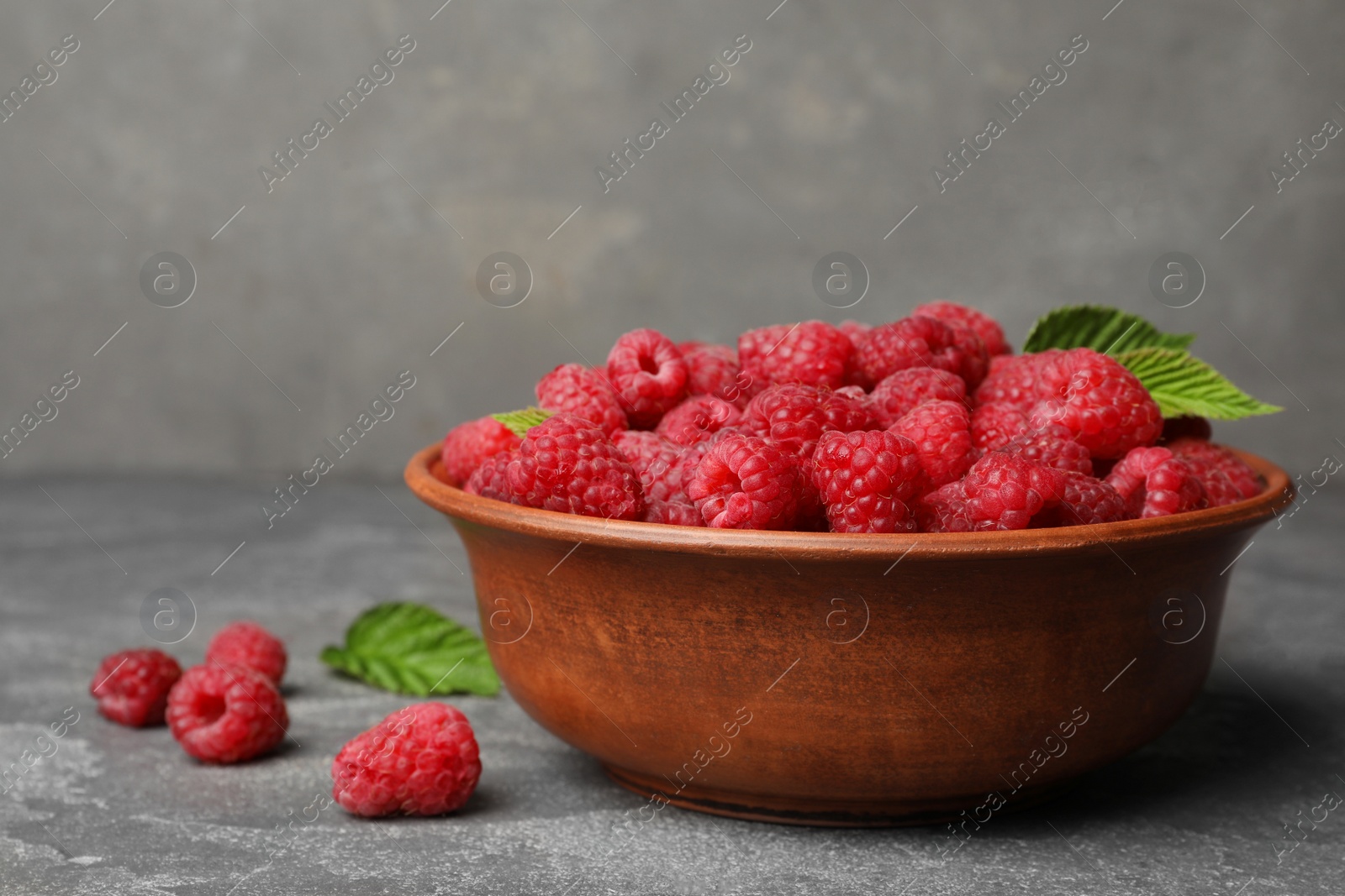 Photo of Bowl with delicious ripe raspberries on stone surface, space for text