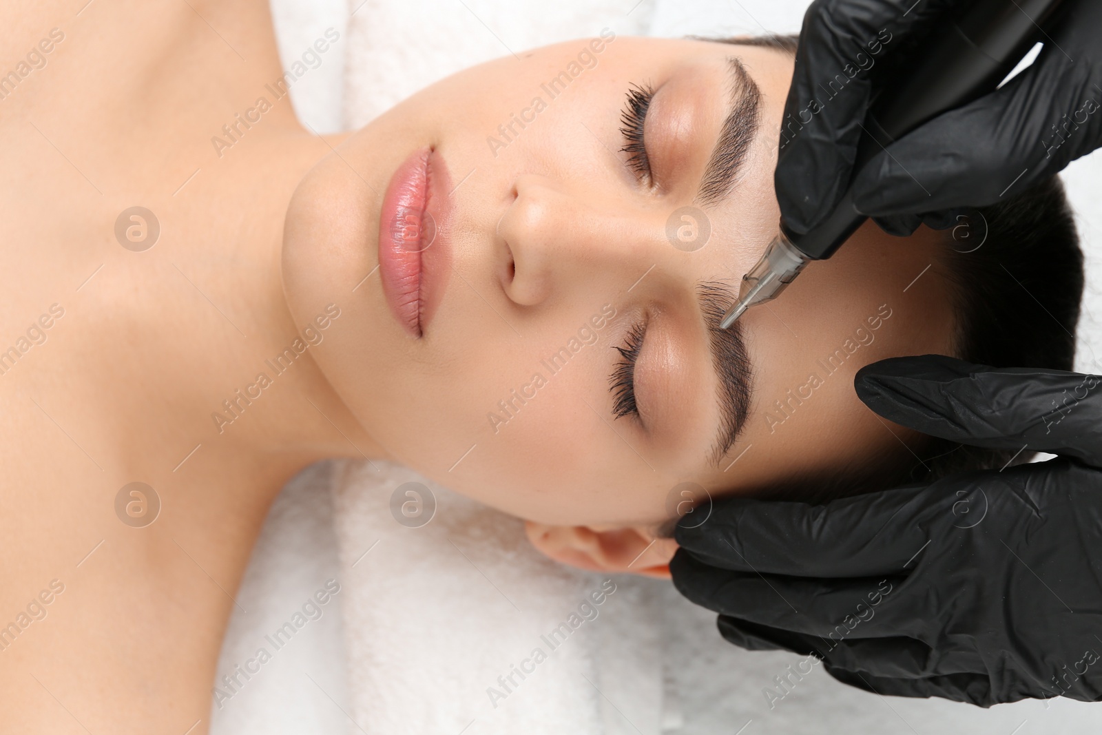 Photo of Beautician making permanent eyebrow makeup to young woman, top view