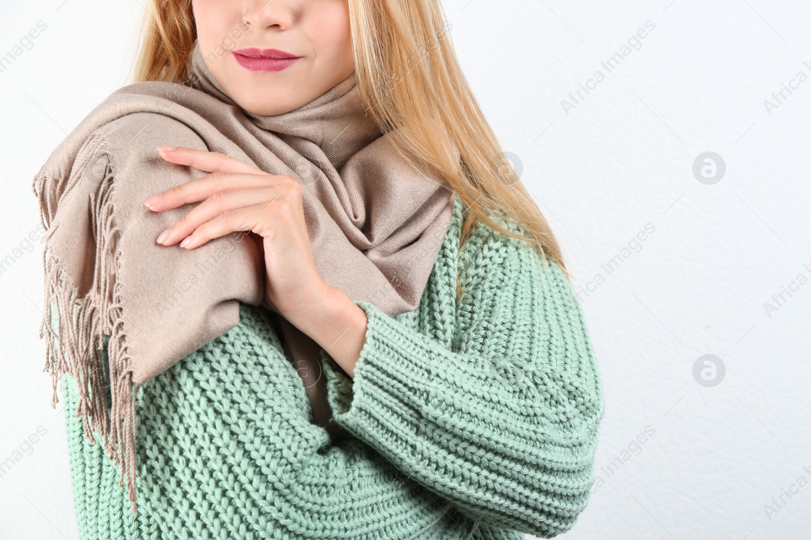 Image of Young woman wearing warm sweater and scarf on white background, closeup