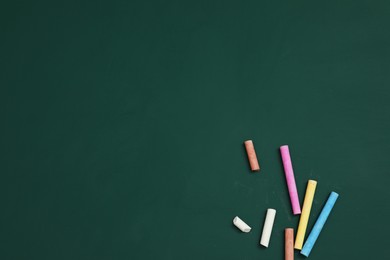 Photo of Colorful chalks on green board, flat lay. Space for text