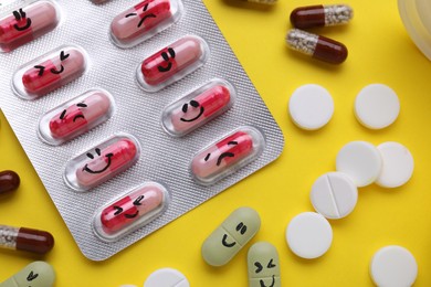 Photo of Different antidepressants with emoticons on yellow background, flat lay