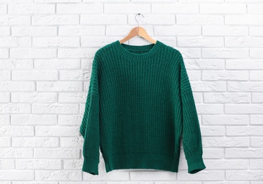 Hanger with stylish sweater on brick wall