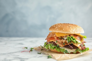 Tasty burger with bacon on table against color background. Space for text