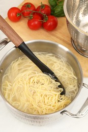 Cooked spaghetti and pasta server in metal pot on white countertop, closeup