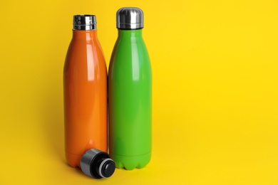 Photo of Stylish stainless thermo bottles on yellow background. Space for text
