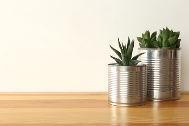 Photo of Houseplants in tin cans on wooden table. Space for text