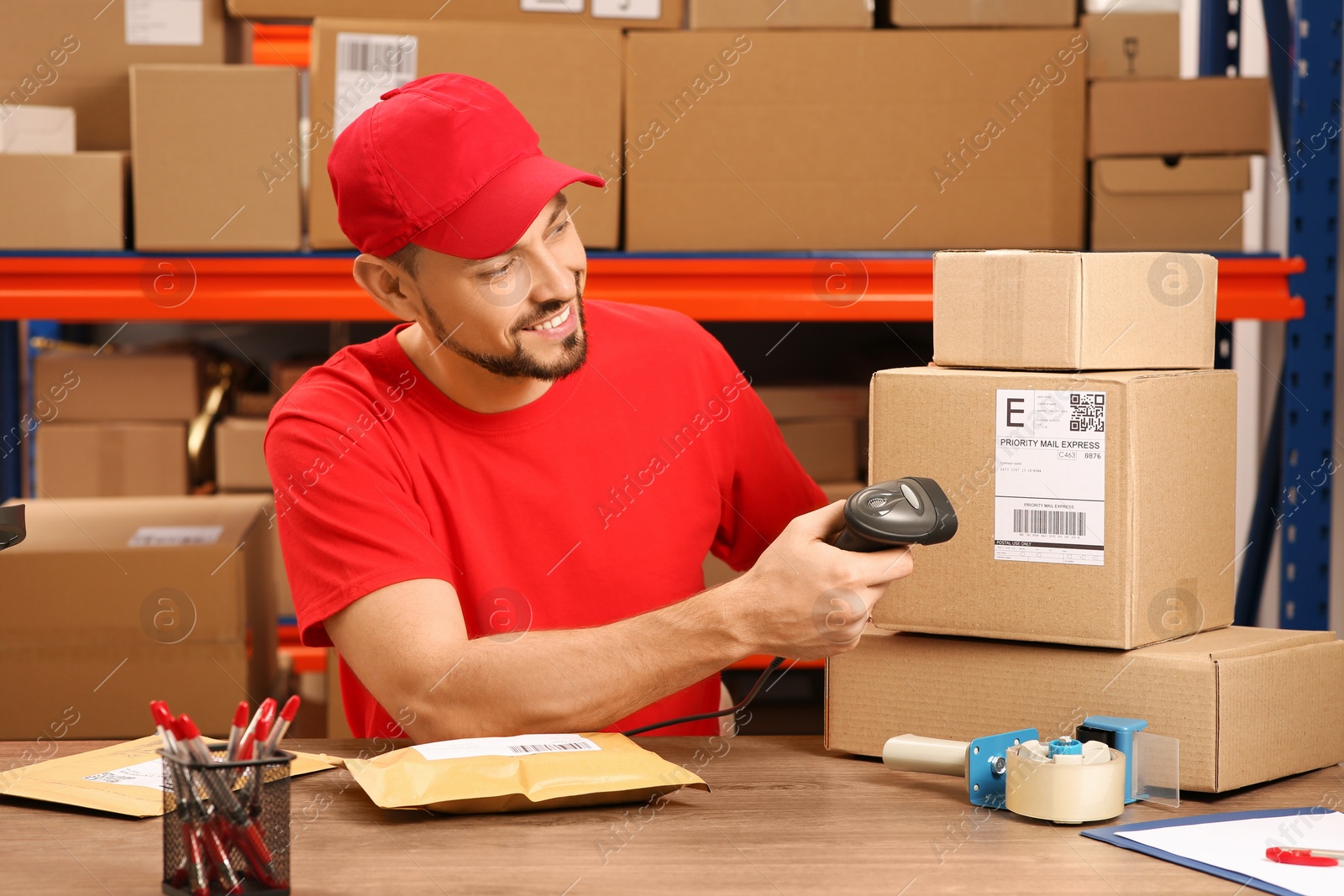 Photo of Post office worker with scanner reading parcel barcode at counter indoors