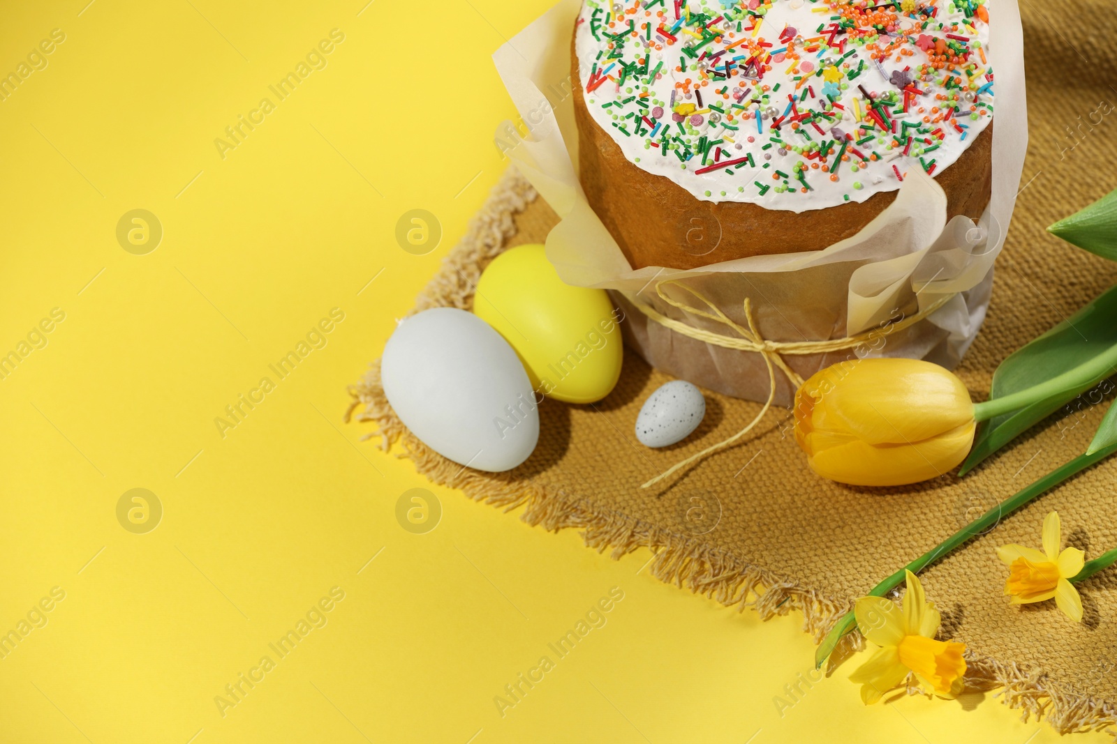 Photo of Traditional Easter cake with sprinkles, decorated eggs and flowers on yellow background. Space for text