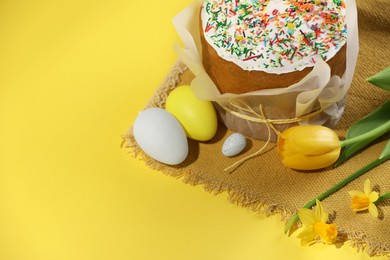 Traditional Easter cake with sprinkles, decorated eggs and flowers on yellow background. Space for text