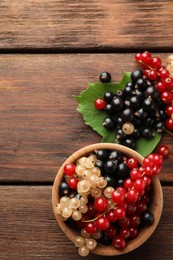 Photo of Different fresh ripe currants and green leaf on wooden table, flat lay. Space for text