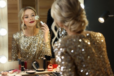 Beautiful makeup. Smiling woman applying powder with brush onto face in front of mirror in dressing room