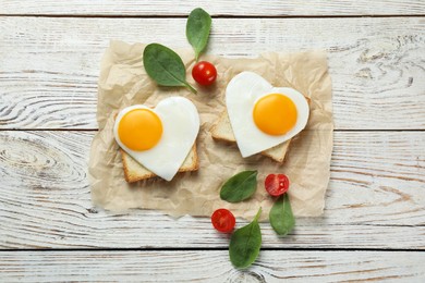 Photo of Heart shaped fried eggs with toasts, spinach and tomatoes on white wooden table, flat lay