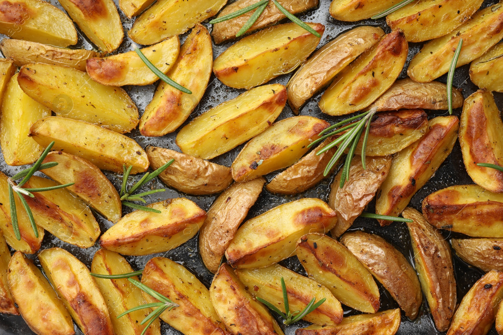 Photo of Delicious baked potatoes with rosemary on black surface, flat lay