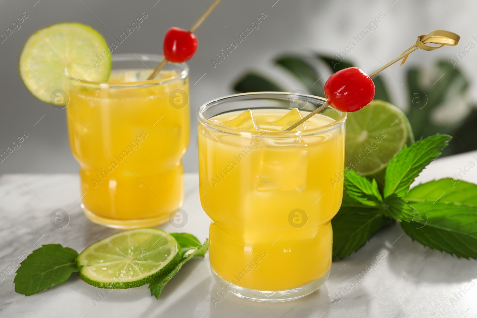 Photo of Glasses of tasty pineapple cocktail with cherry, lime and mint on white table, closeup