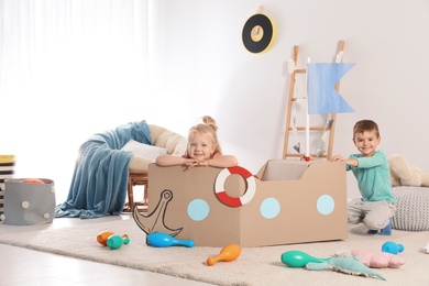 Photo of Cute little children playing with cardboard ship at home