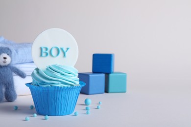 Photo of Beautifully decorated baby shower cupcake with cream and boy topper on light grey background. Space for text