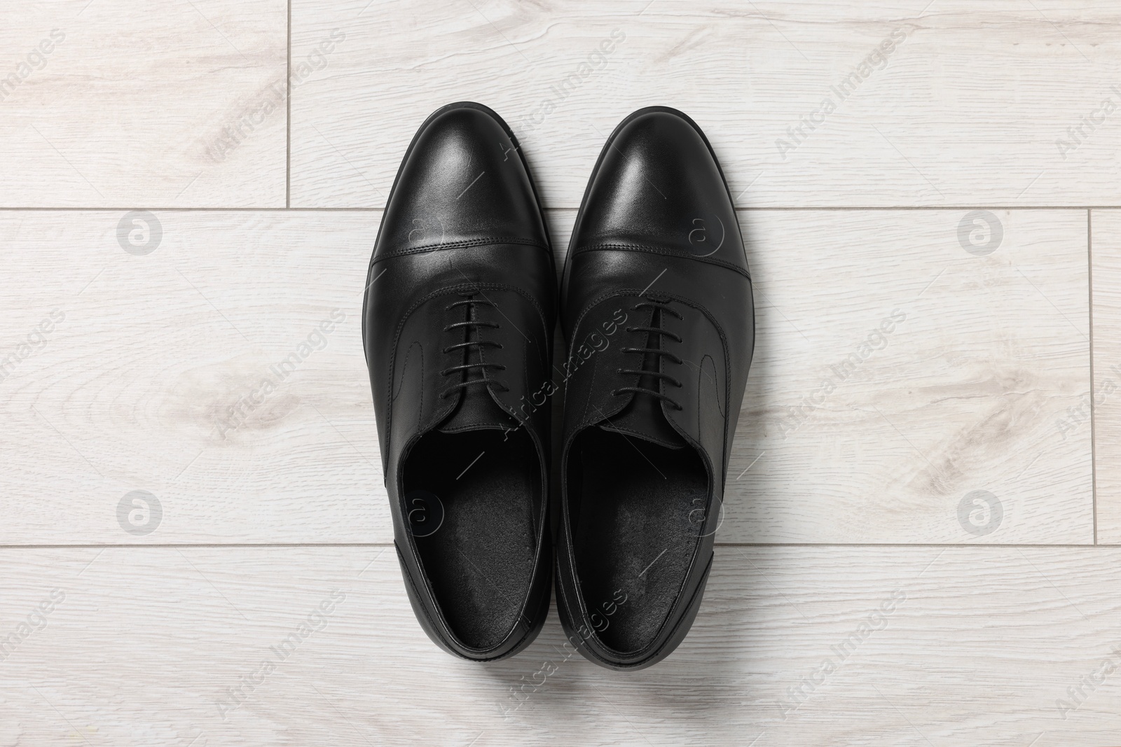 Photo of Pair of black leather men shoes on light wooden floor, top view