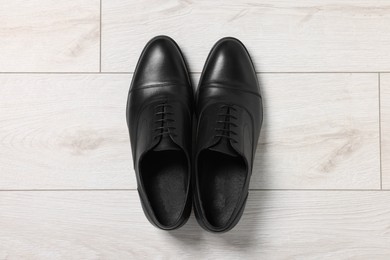 Photo of Pair of black leather men shoes on light wooden floor, top view