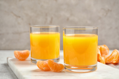 Glasses of fresh tangerine juice and fruits on light table