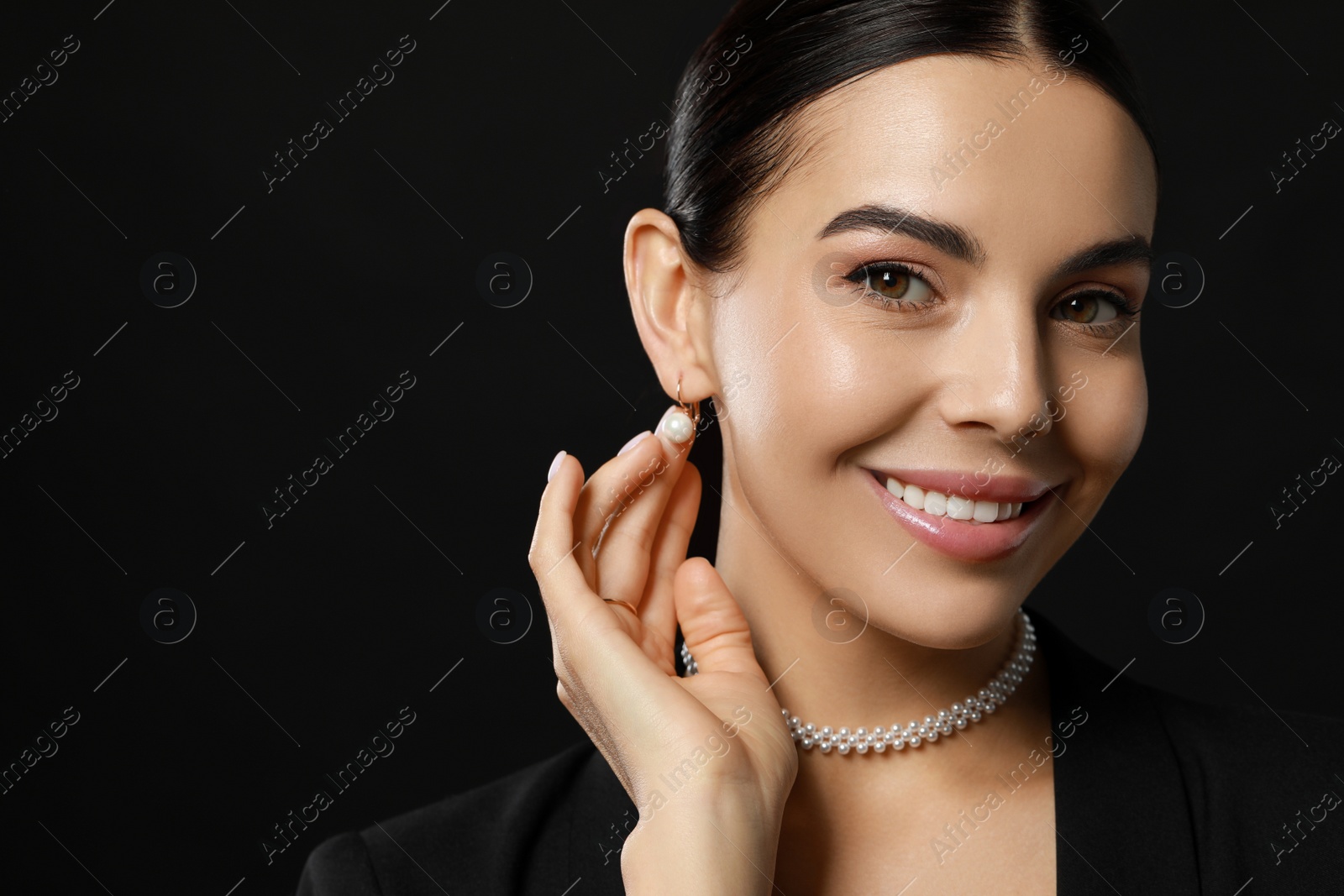 Photo of Young woman with elegant pearl jewelry on black background, closeup. Space for text