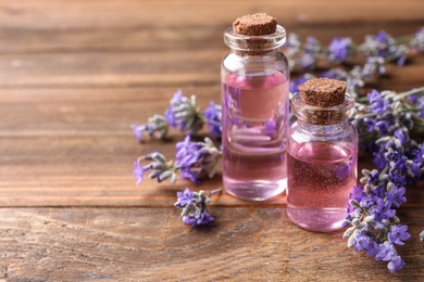 Photo of Bottles with natural lavender oil and flowers on wooden table, closeup view. Space for text