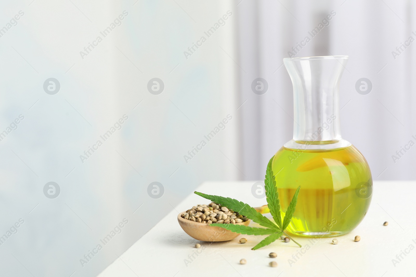 Photo of Bottle with hemp oil, leaf and seeds on white table indoors. Space for text