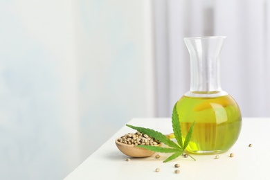 Bottle with hemp oil, leaf and seeds on white table indoors. Space for text