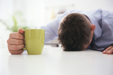 Man with cup of drink sleeping at home in morning, focus on hand
