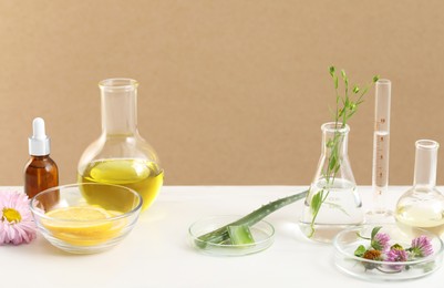 Developing cosmetic oil. Laboratory glassware and flowers on white table