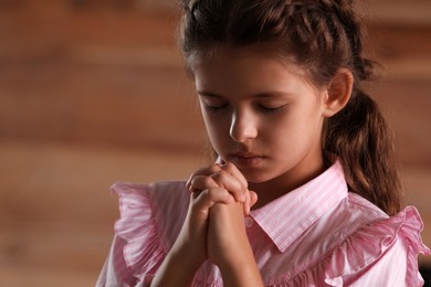 Photo of Cute little girl with hands clasped together praying on blurred background