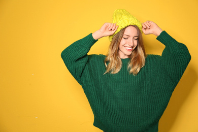 Happy young woman wearing warm sweater and knitted hat on yellow background 