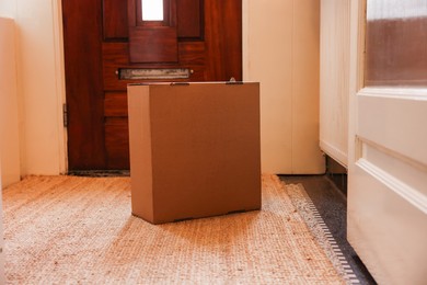 Photo of Delivery service. Cardboard on rug near wooden door indoors