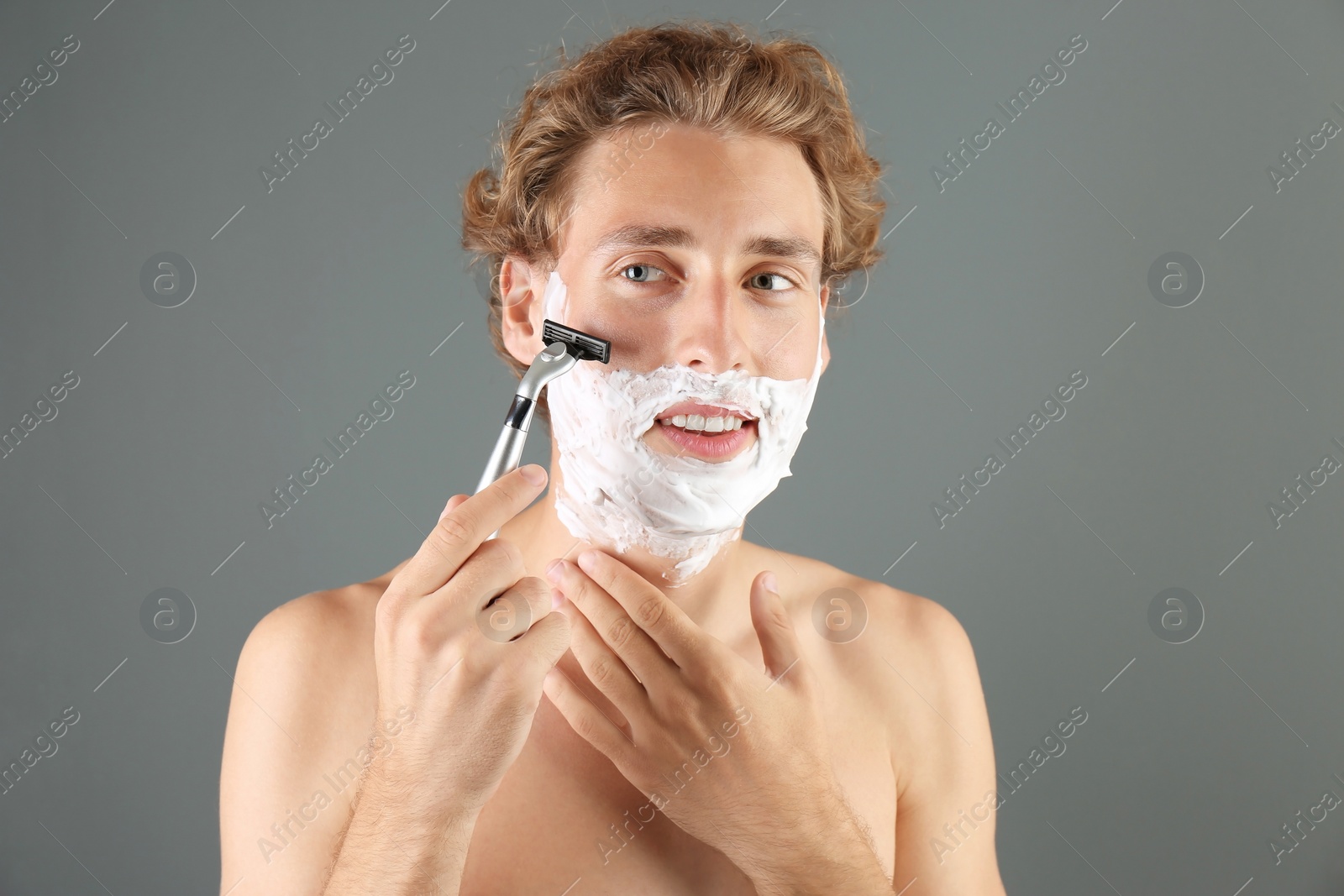 Photo of Handsome young man shaving on gray background