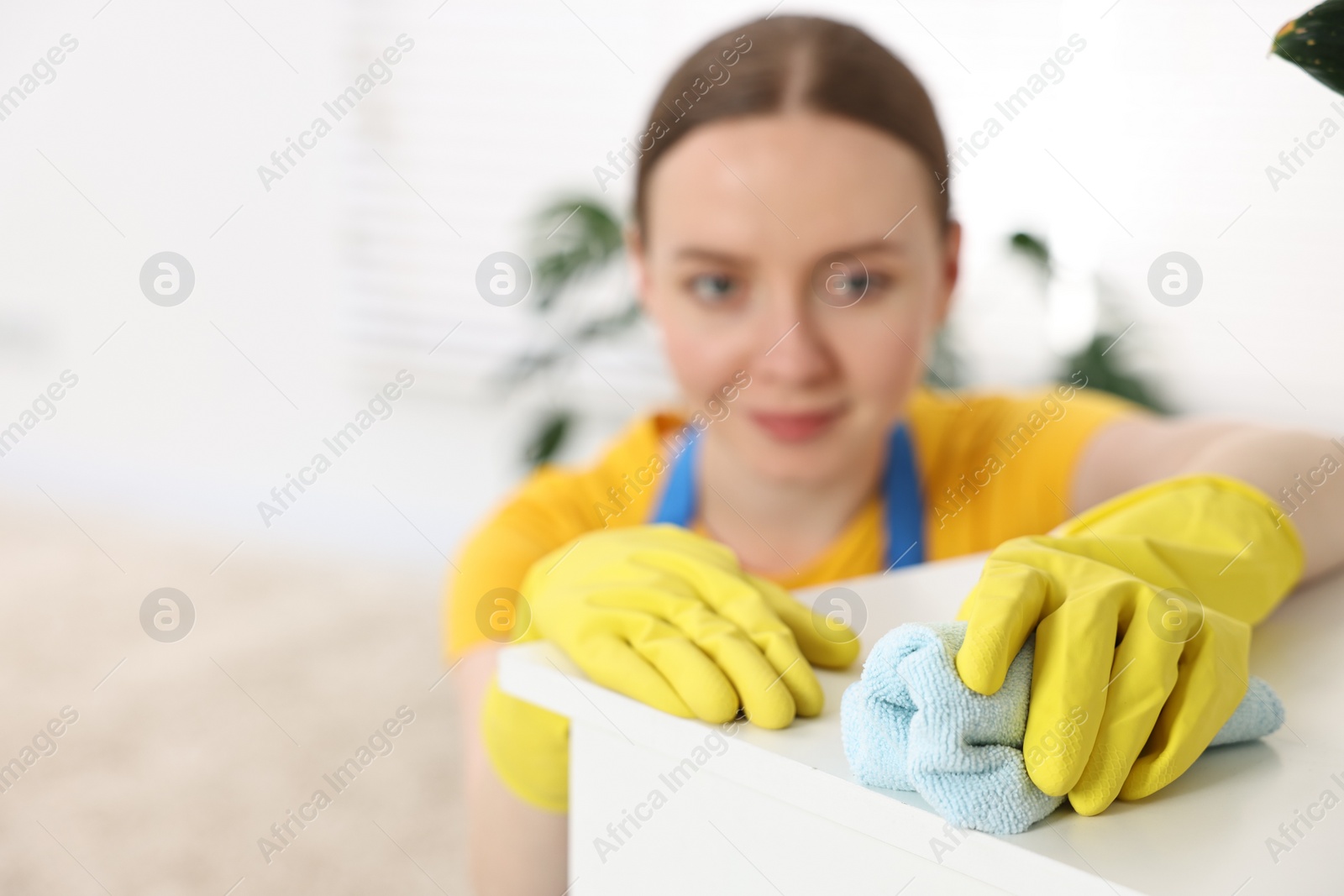 Photo of Woman cleaning table with rag at home, selective focus. Space for text