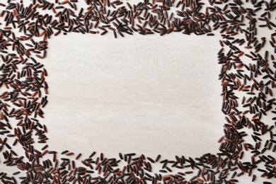 Frame made with black rice on white wooden background, top view. Space for text