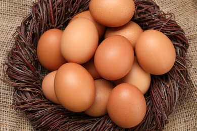 Photo of Fresh chicken eggs in nest on burlap fabric, top view