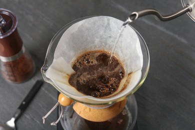 Photo of Pouring hot water into glass chemex coffeemaker with paper filter and coffee on gray table, above view