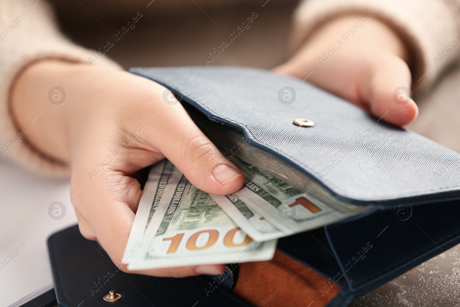 Photo of Woman putting money into wallet at brown table, closeup