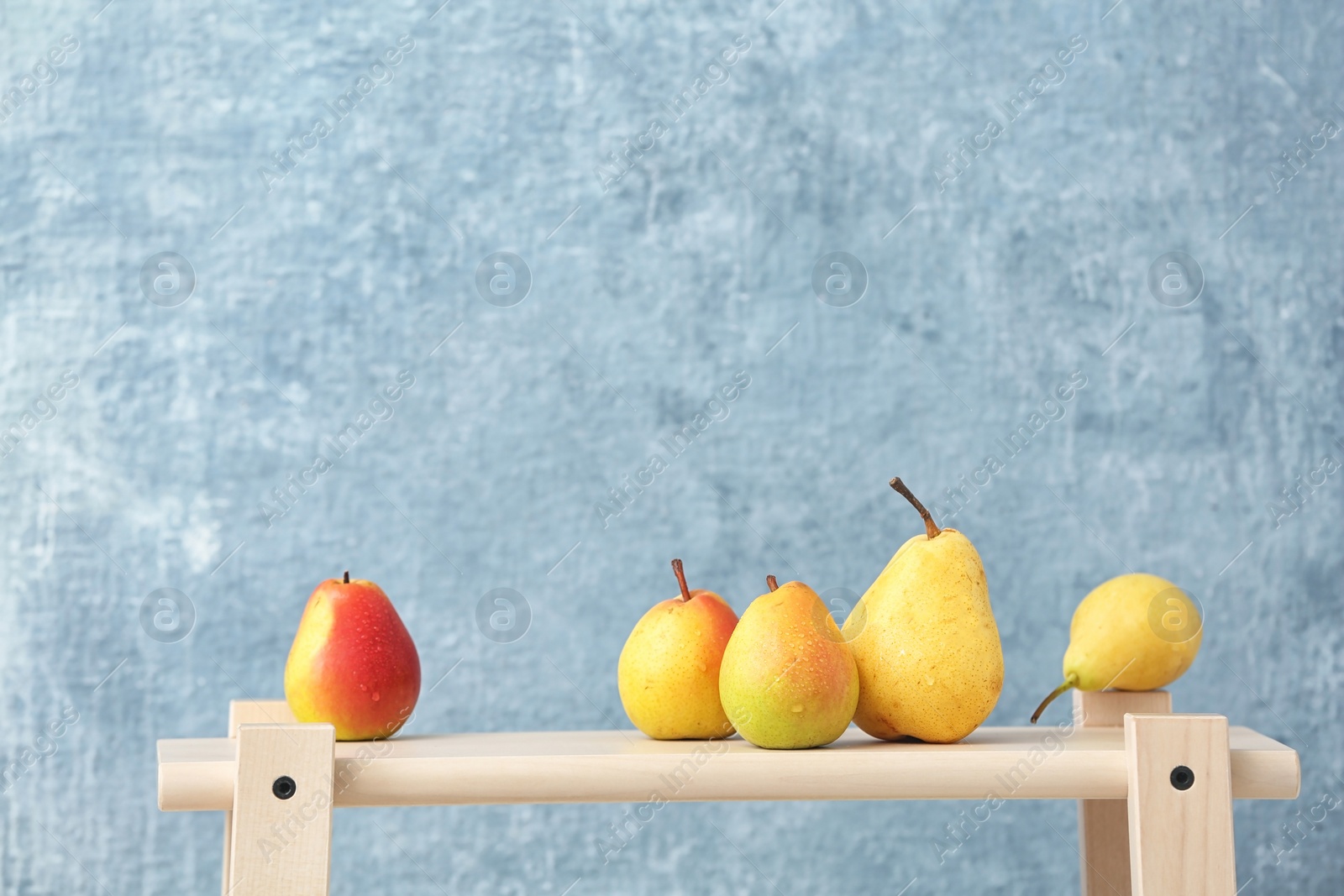 Photo of Ripe pears on wooden table against color background. Space for text