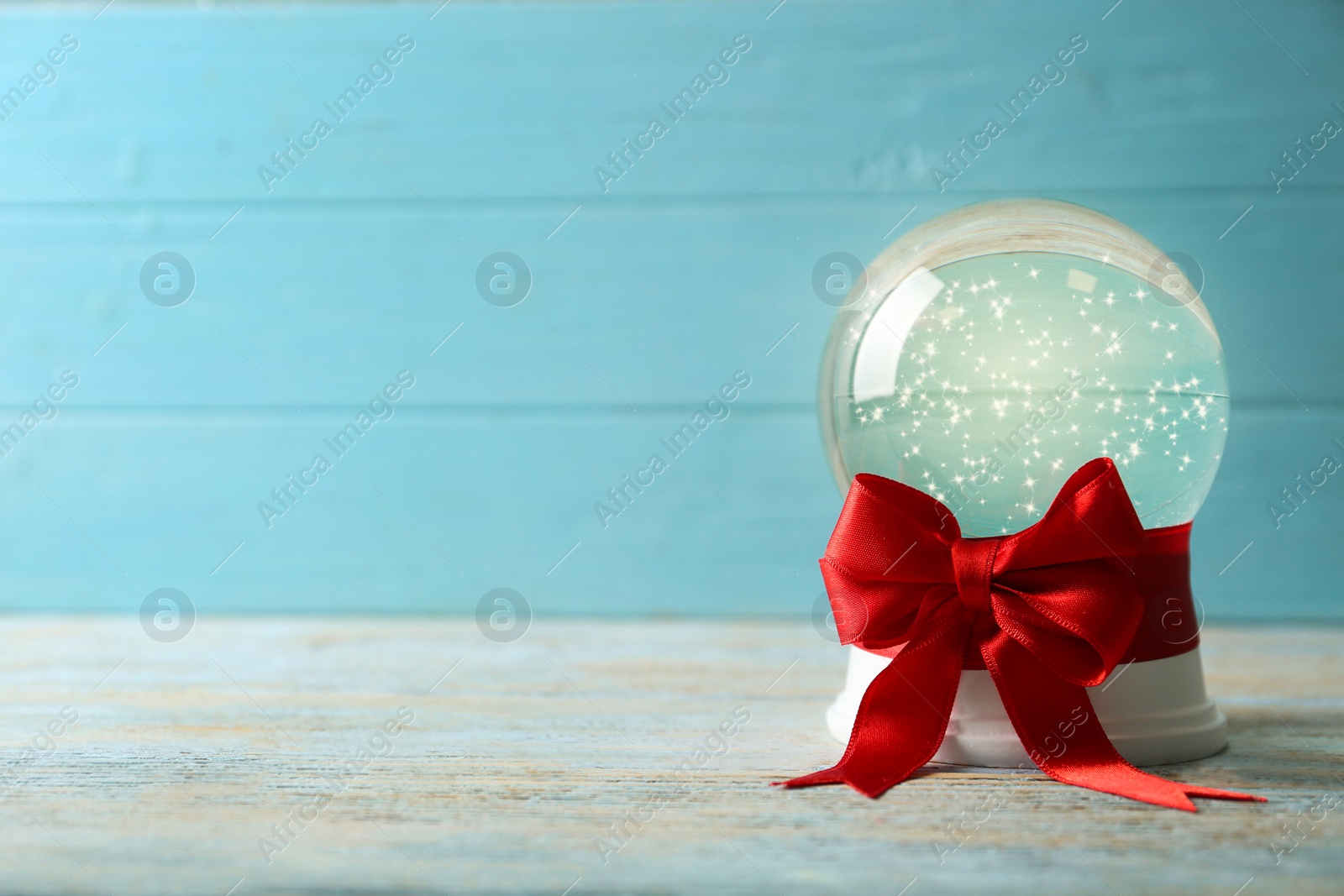 Photo of Beautiful Christmas snow globe with red bow on white wooden table against blue background, space for text