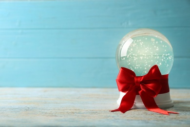 Beautiful Christmas snow globe with red bow on white wooden table against blue background, space for text