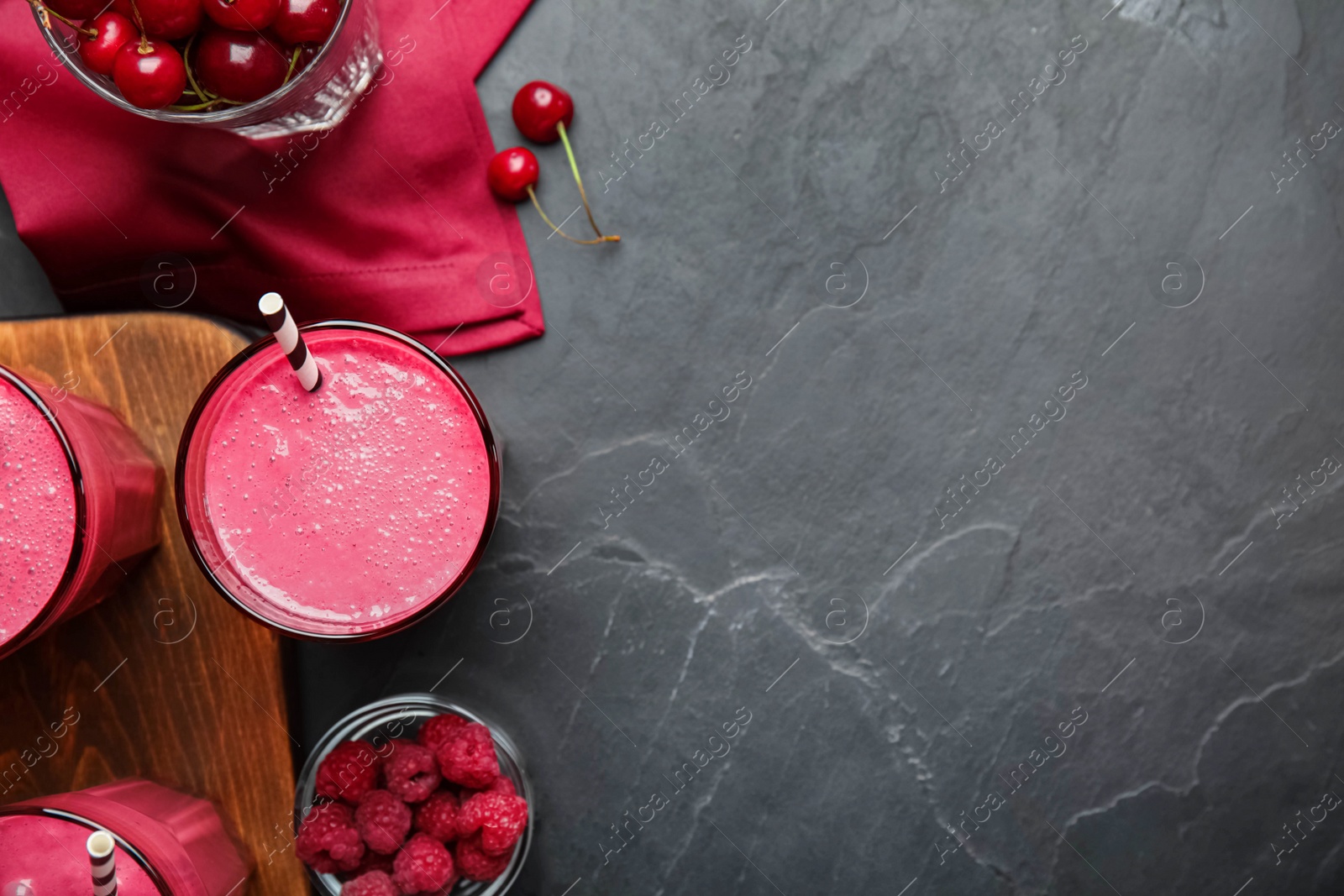 Photo of Tasty fresh milk shakes with berries on black table, flat lay. Space for text